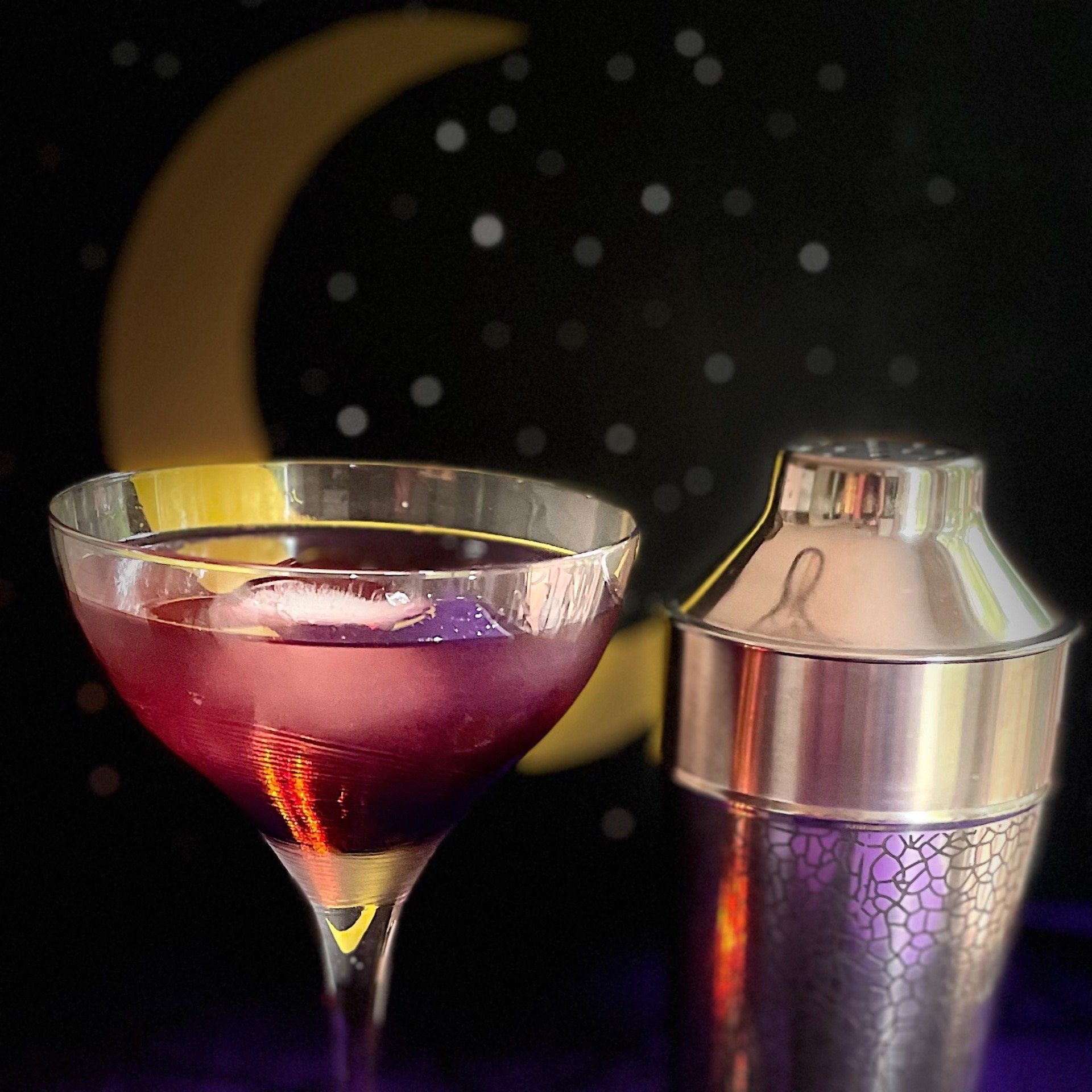 Stunning dark purple total solar eclipse cocktail with edible glitter for stars and spherical ice for moon.